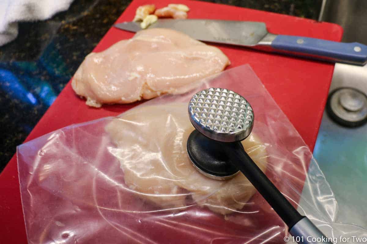 flattening thick chicken breast in a plastic bag with a meat mallet