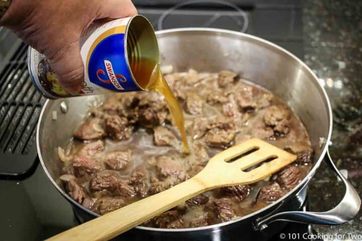 pouring beef broth into skillet with browned meat