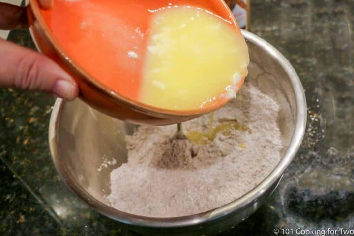 adding melted butter to flour in metal bowl