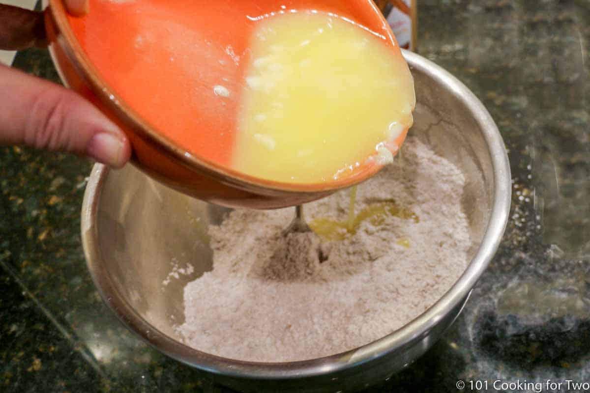 adding melted butter to flour in metal bowl