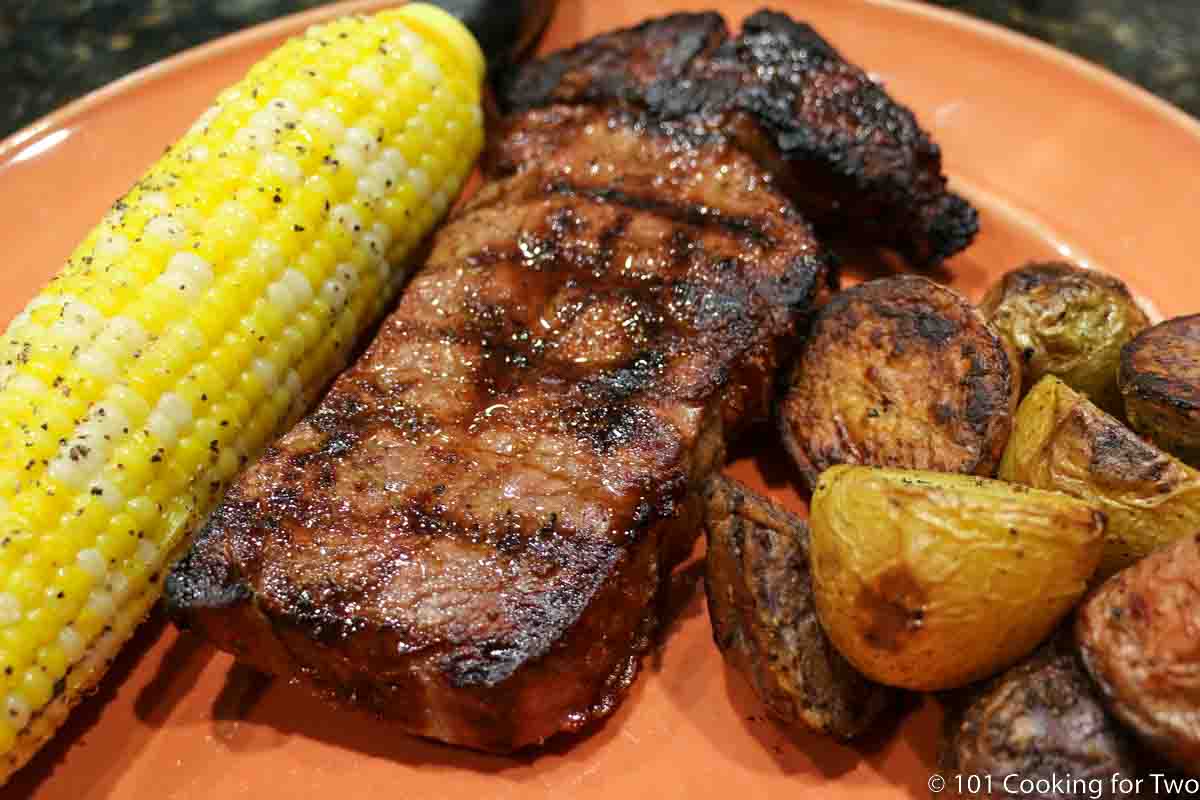 cooked ribeye steak with corn and potatoes on orange plate.