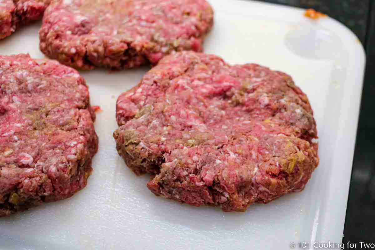 forming ground beef mixture into patties with a dimple on a white board.
