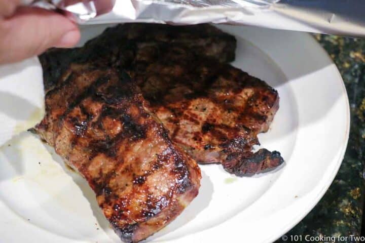 tenting a ribeye with foil on a white plate