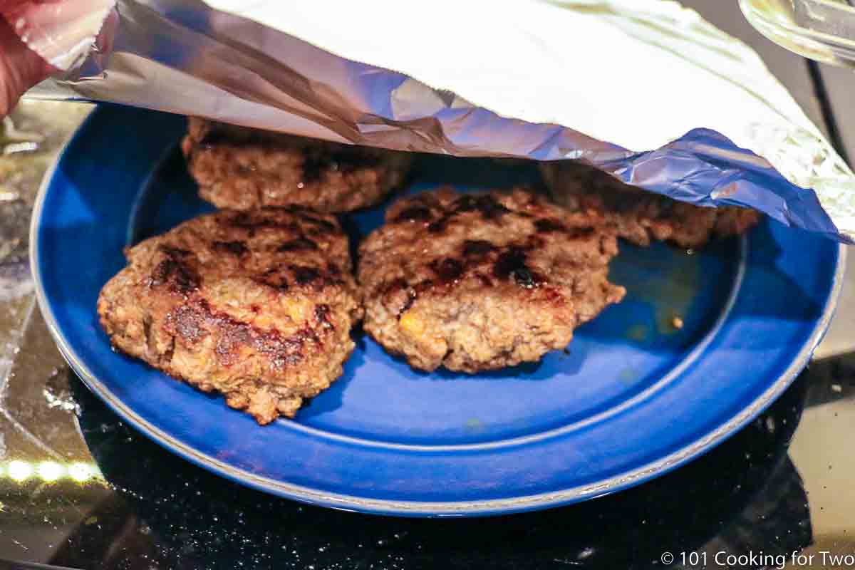 tenting the cooked patties on blue plate.