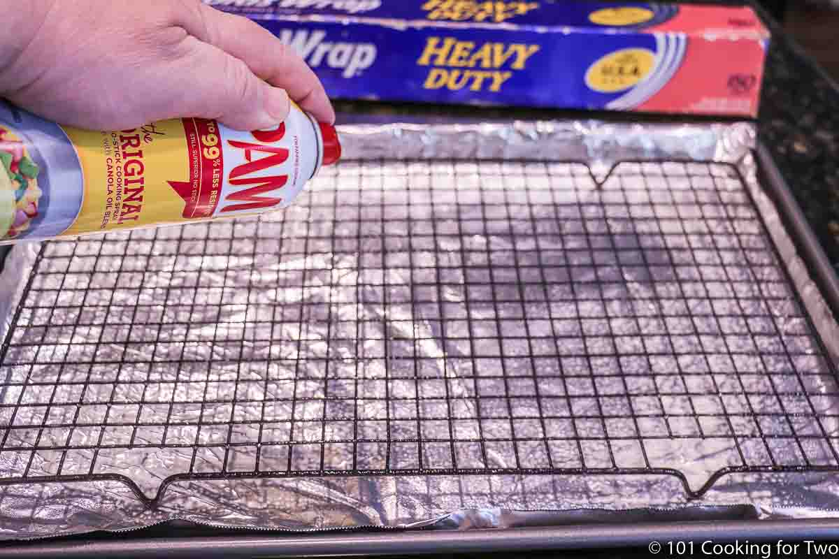 Spraying PAM on a rack on a foil covered tray.