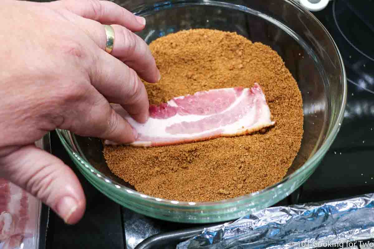 dipping half a raw bacon strip in spice mixture