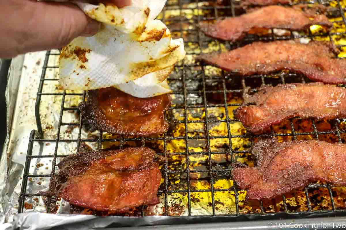 patting off the fat from cooked candied bacon still on the rack