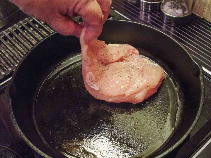 placing chicken breast into cast iron skillet