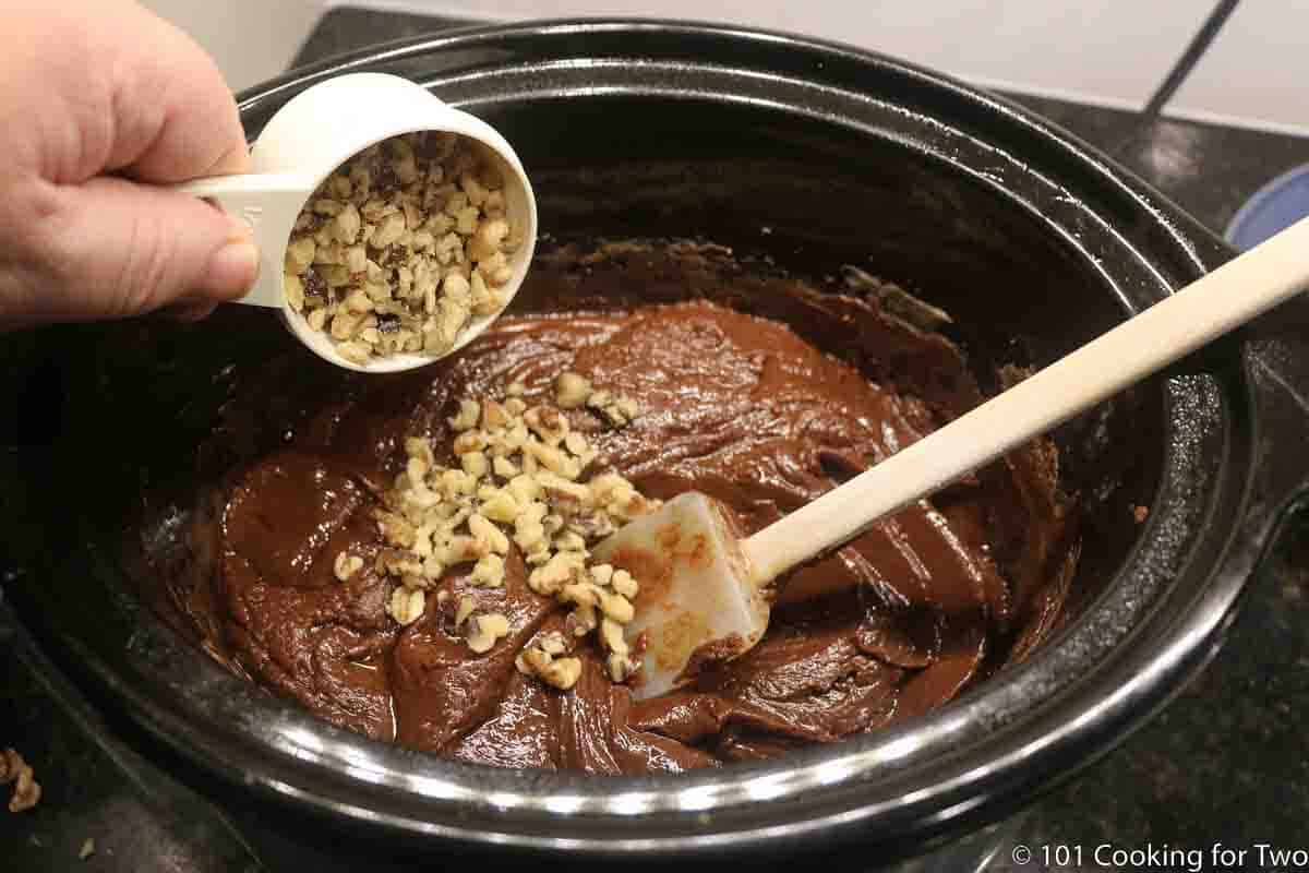 pouring nuts into crock pot with melted fudge.