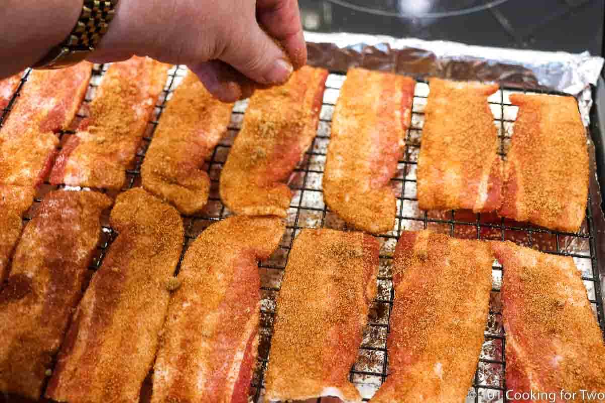 sprinkling extra coating on bacon strips on rack