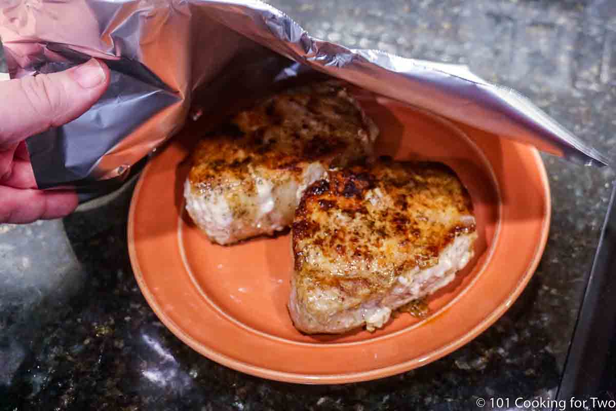 tenting pork chops on orange plate with foil.