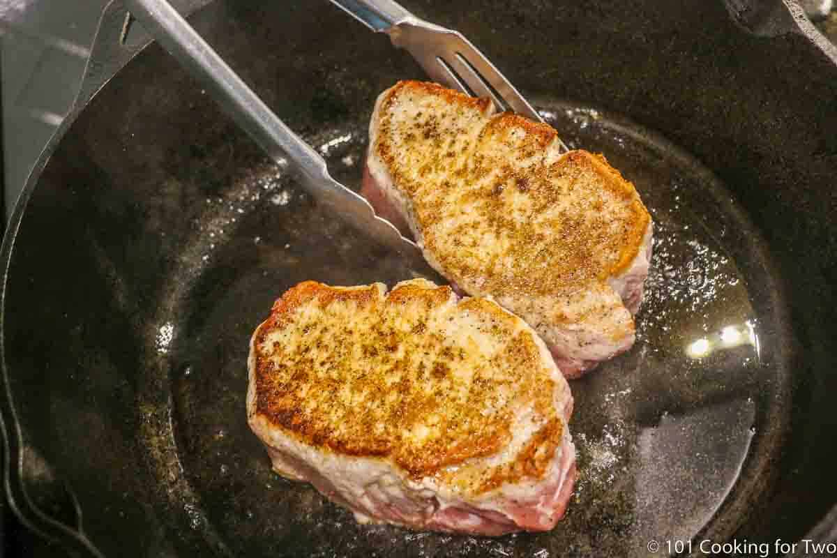 thick pork chops searing in cast iron skillet.