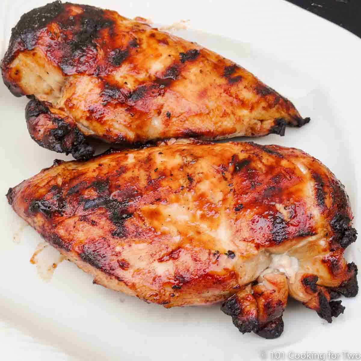 Two BBQ chicken breasts on white plate.