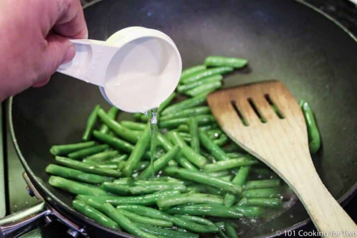 adding water to a pan with green beans