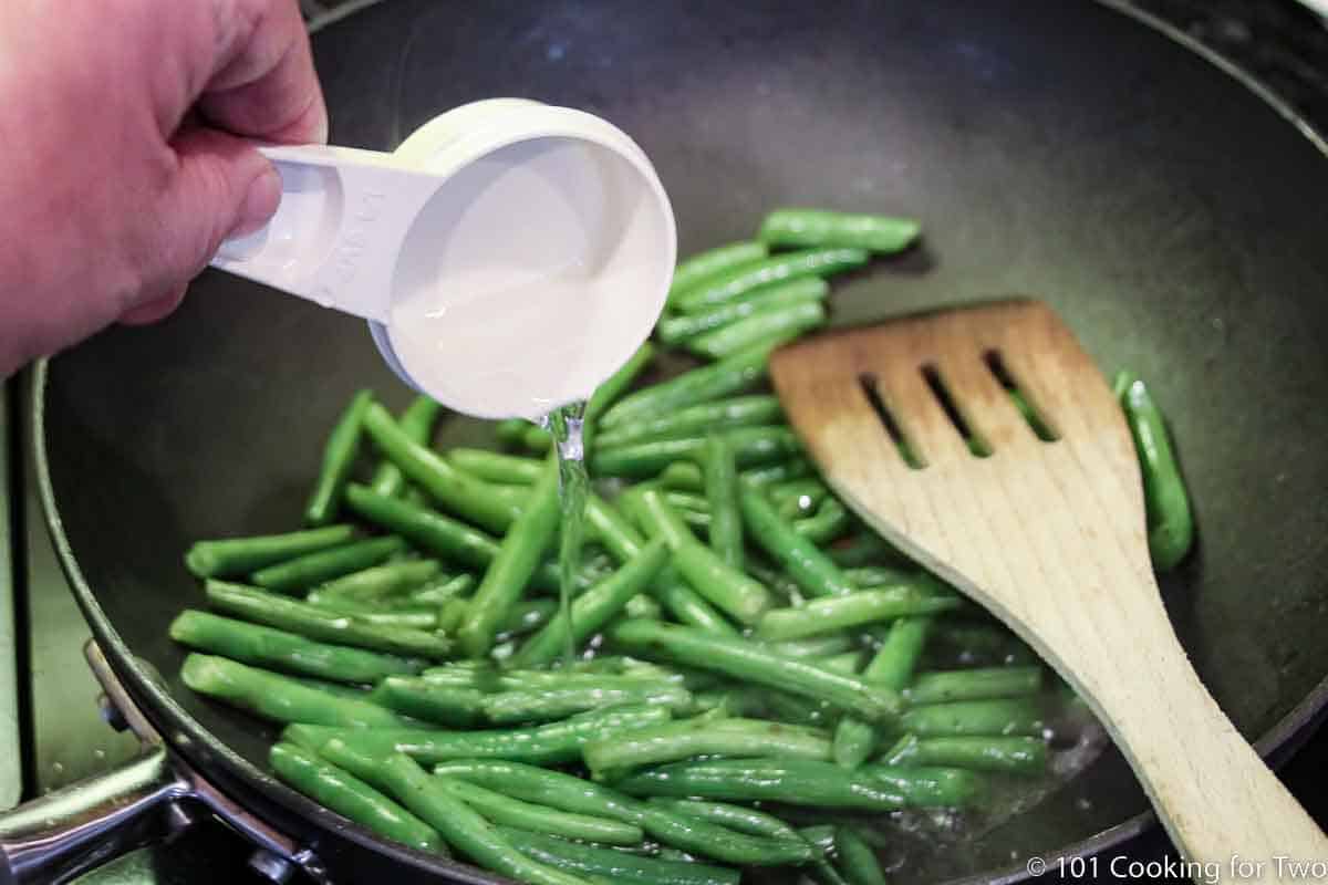 adding water to a pan with green beans.