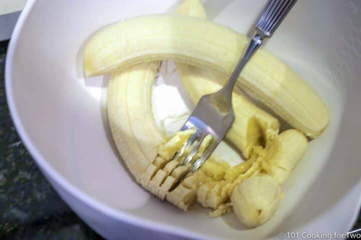 mashing bananas with a fork in a white bowl