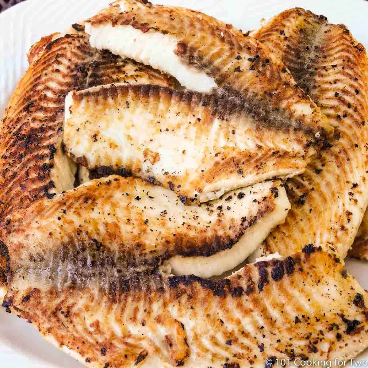 pile of grilled tilapia on white plate.