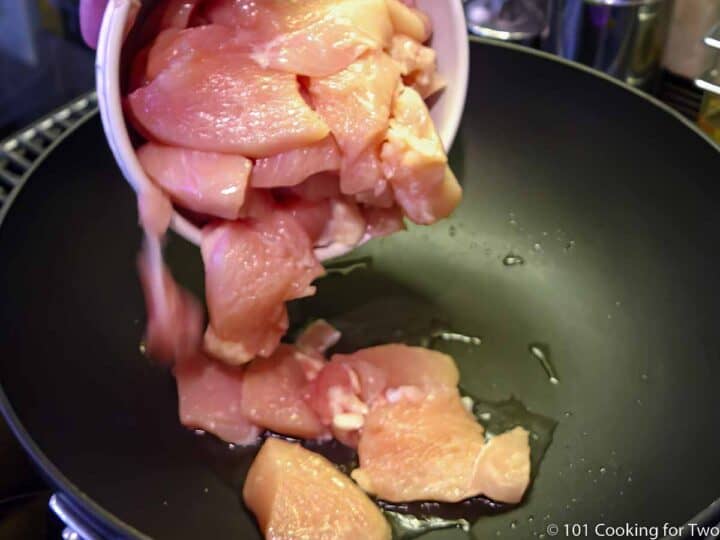 pouring trimmed raw chicken into black skillet with oil