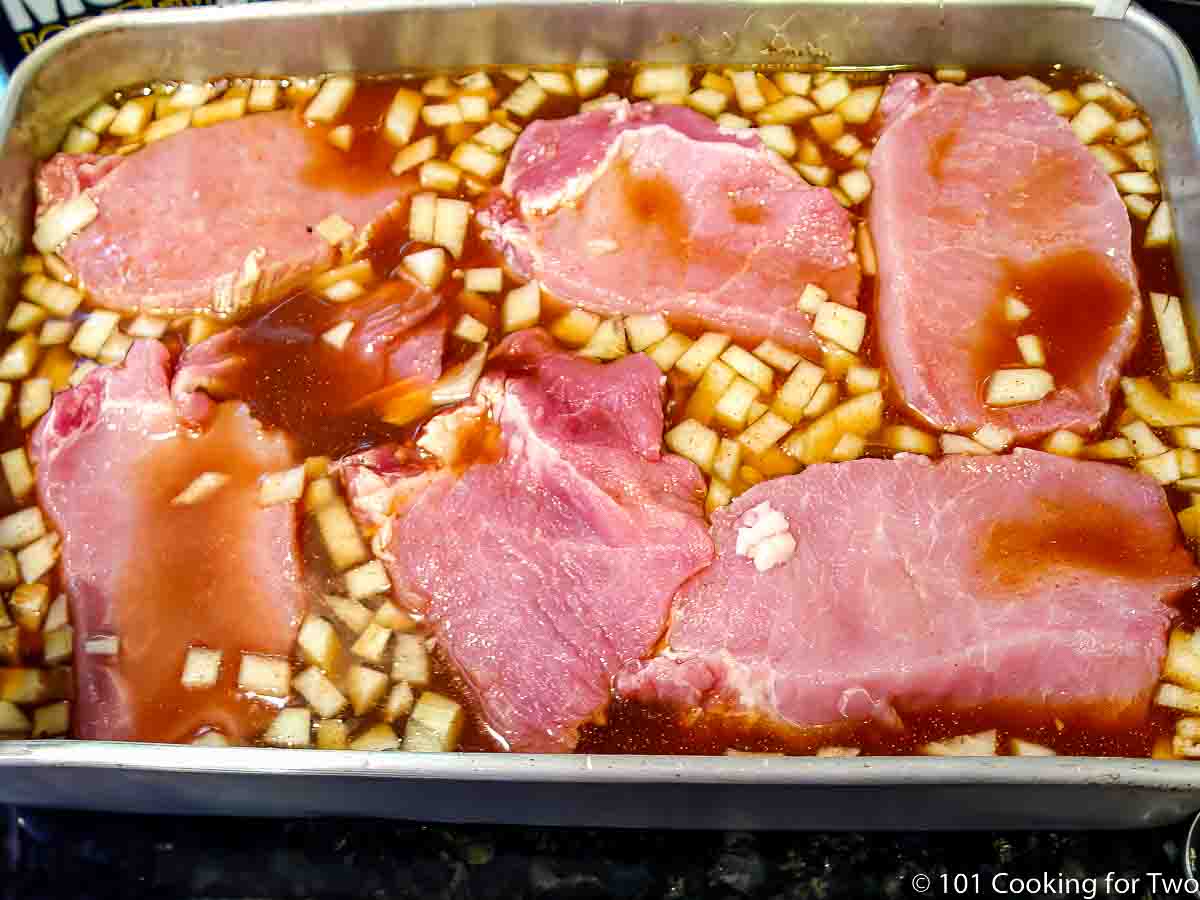 slices of pork loin in a cake pan with braising fluid.