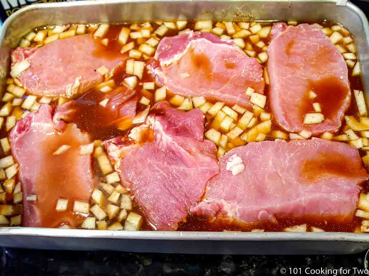 slices of pork loin in a cake pan with braising fluid.