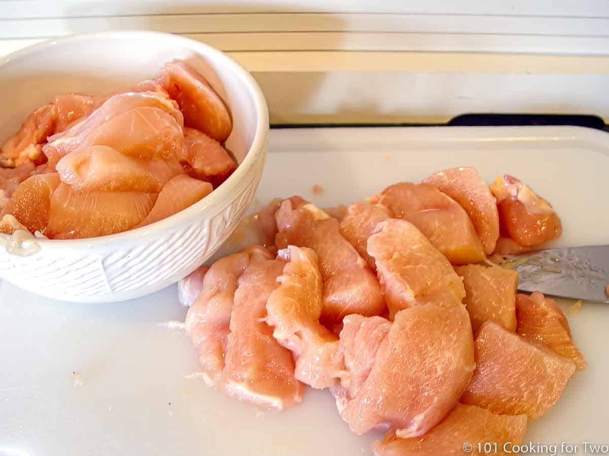 trim and sliced chicken breast on a white board.