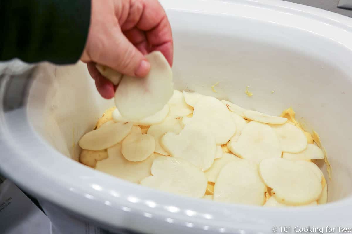 adding slices of potato to crock pot.