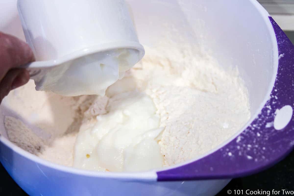 adding yogurt to biscuit ingredients in white bowl.