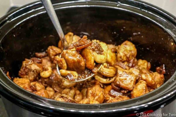 cashew chicken in ladle over a crock pot
