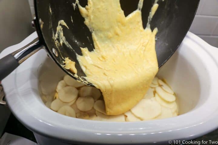 pouring cheese sauce over potato slices
