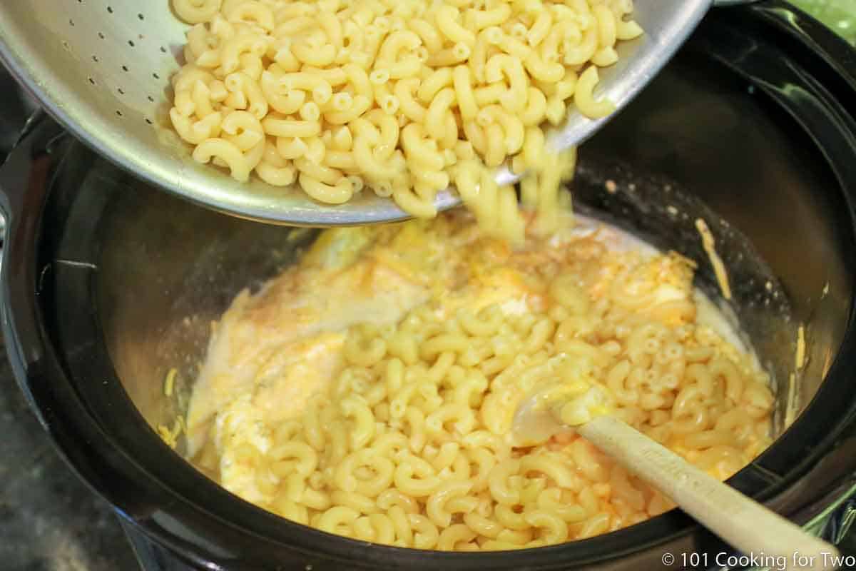 pouring cooked pasta into crock pot.