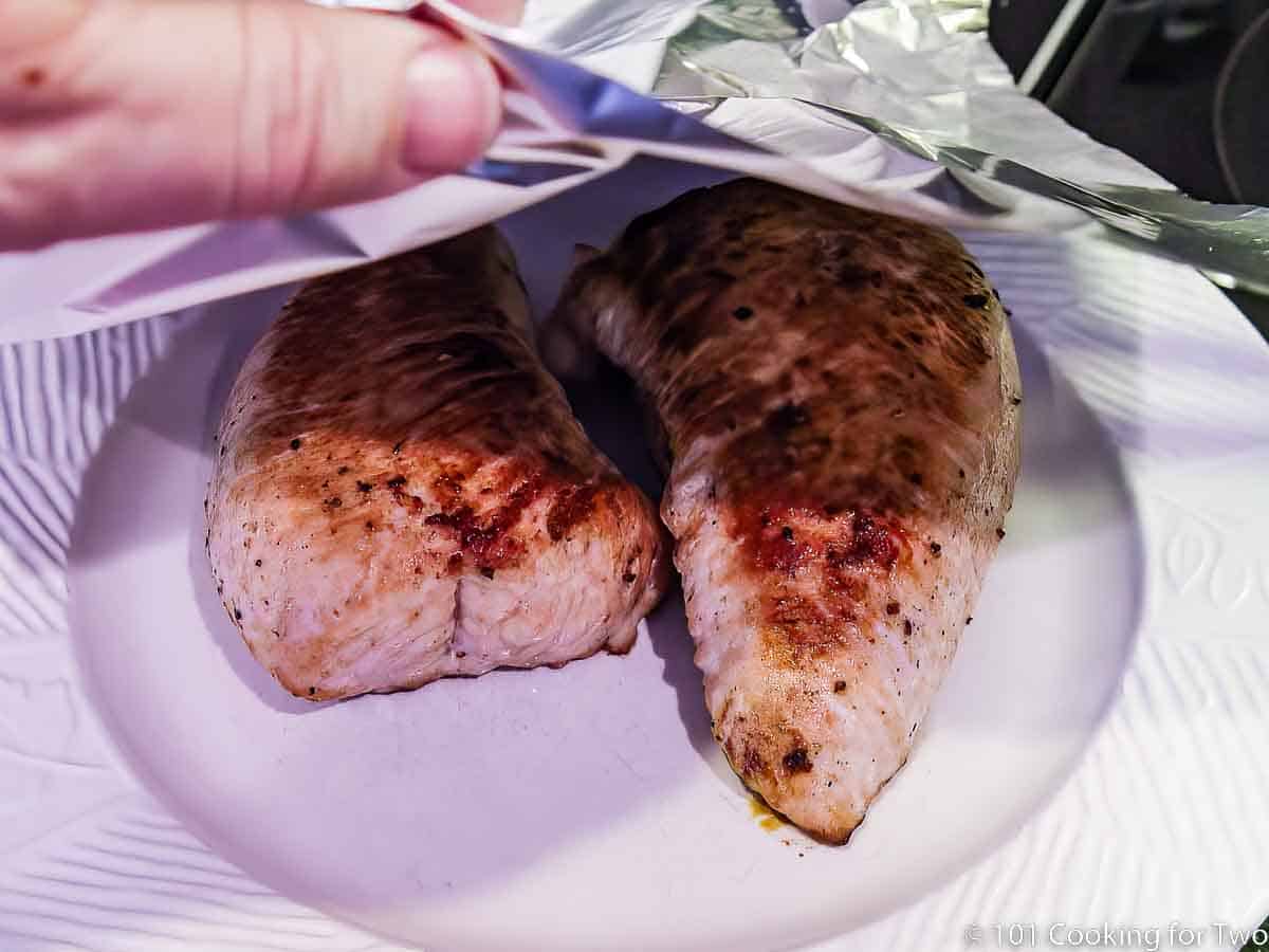 tenting turkey tenderloins with foil on white plate.