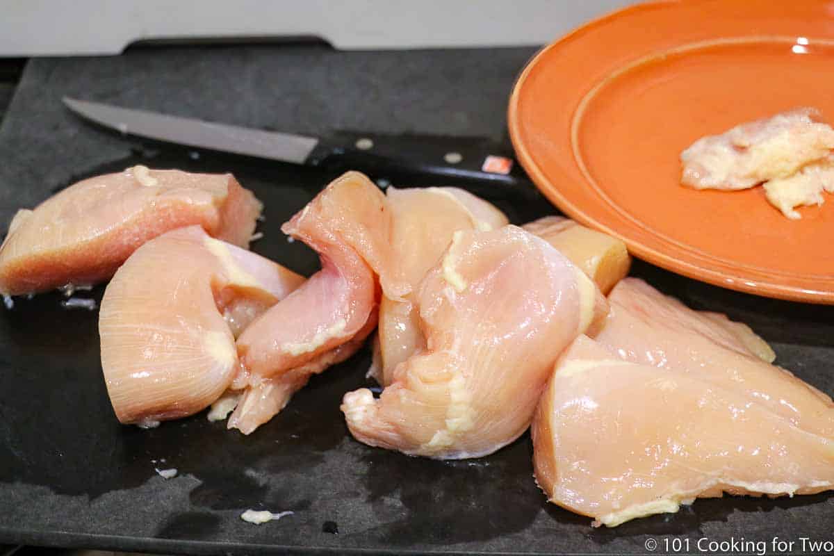 trimmed and cut up chicken breasts on a black board.