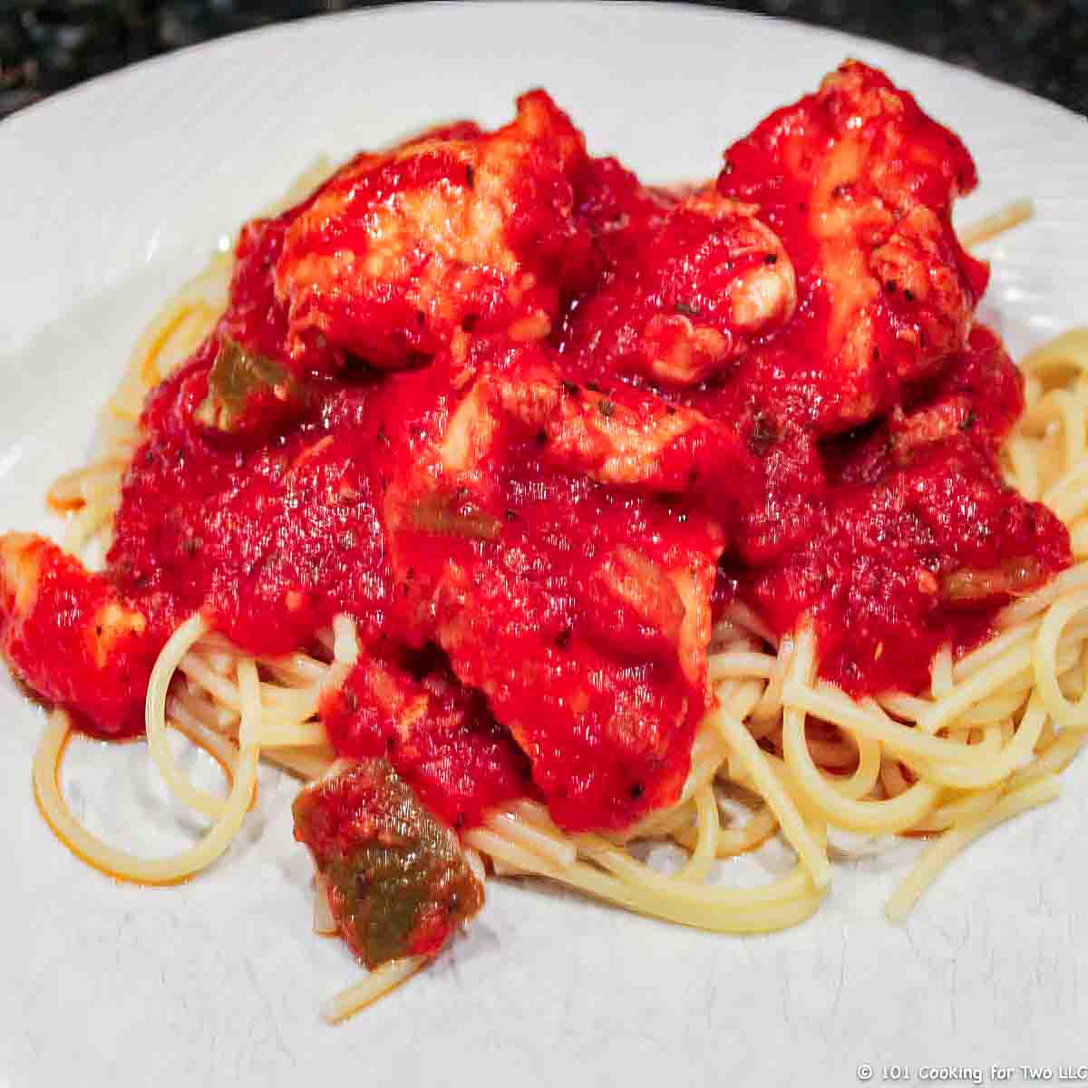 chicken cacciatore on pasta and on white plate.