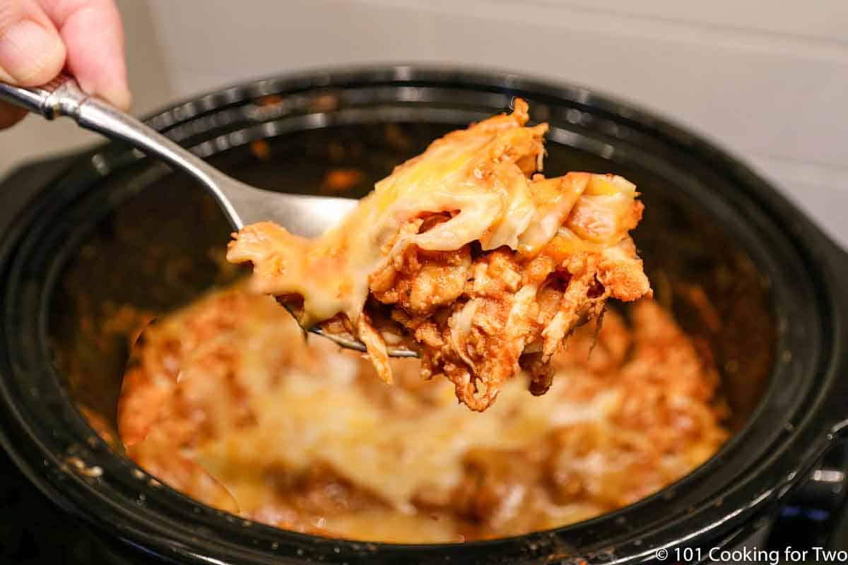 crock pot chicken enchiladas on spoon over the crock pot.