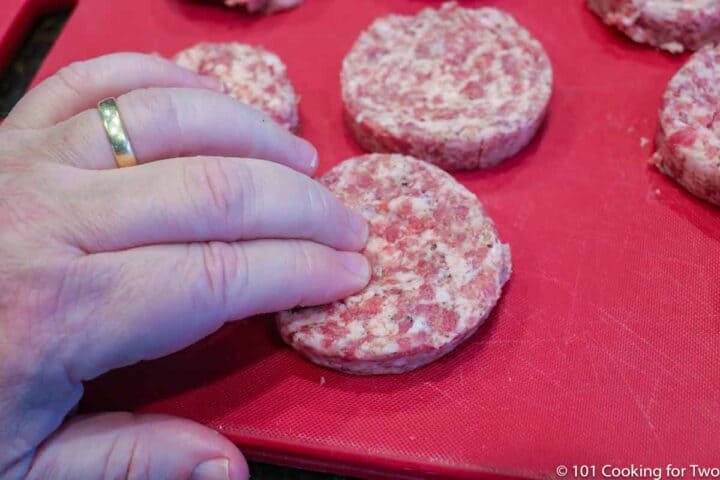 dimpling the center of a sausage pattie on a red board