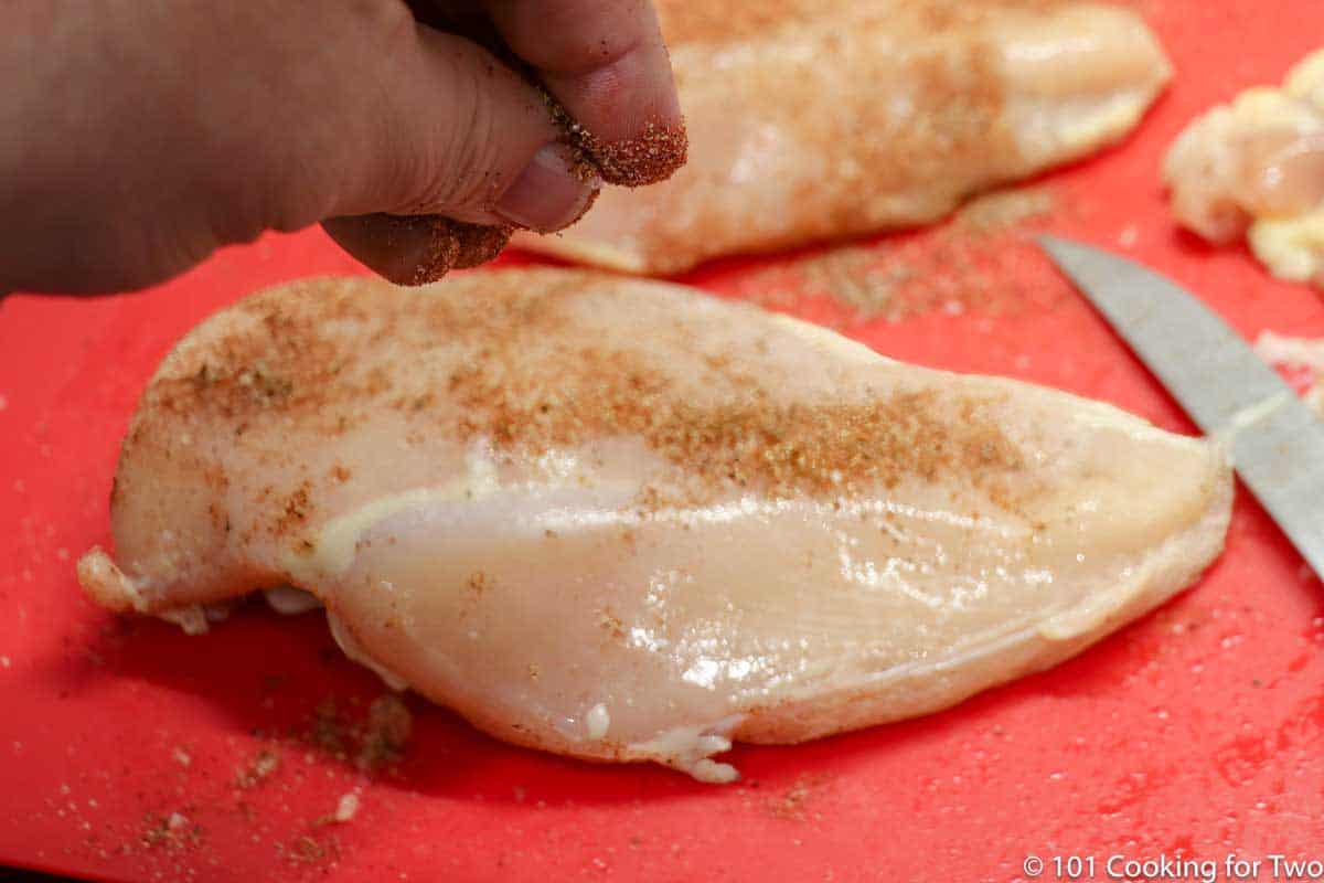 sprnkling spice mix on chicken breasts