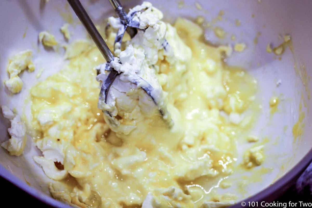 Beating cream cheese batter in a white bowl.