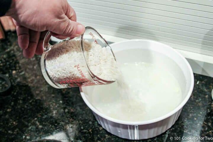 adding long grain rice to water in the baking dish