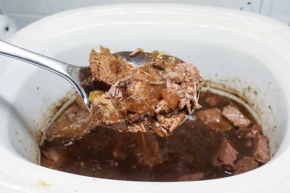 shredded beef in a large spoon over crock pot.