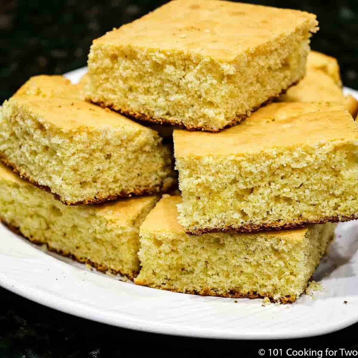 Pile of cornbread slices on a white plate.