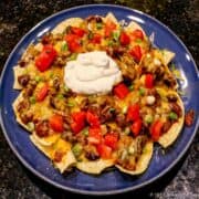 plate of cheese chili nachos topped with tomatos and sour cream