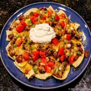 plate of cheese chili nachos topped with tomatos and sour cream