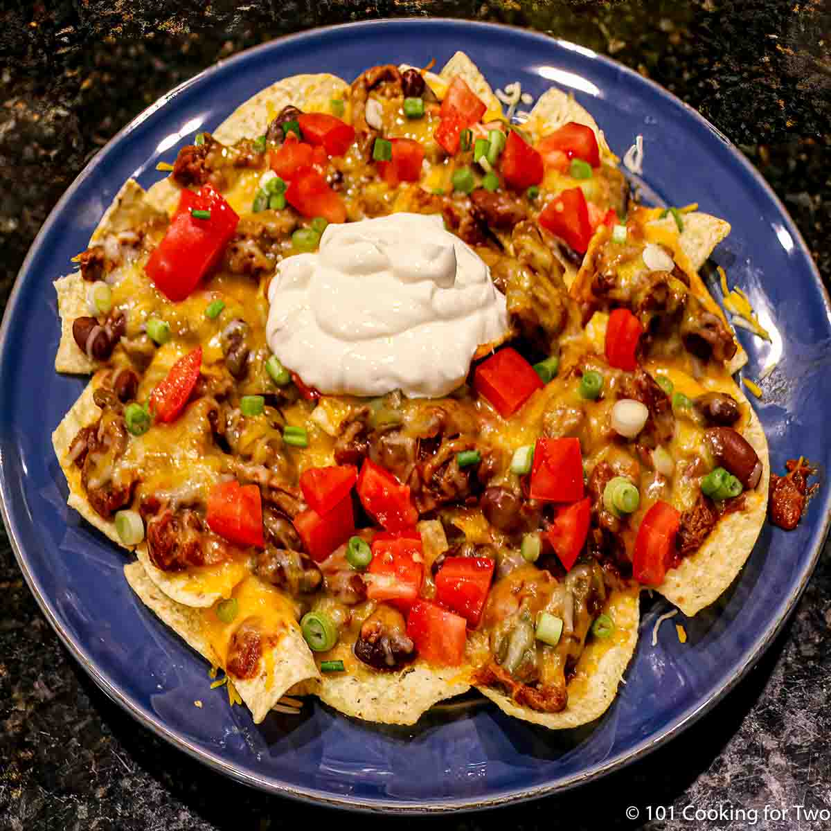plate of cheese chili nachos topped with tomatos and sour cream.