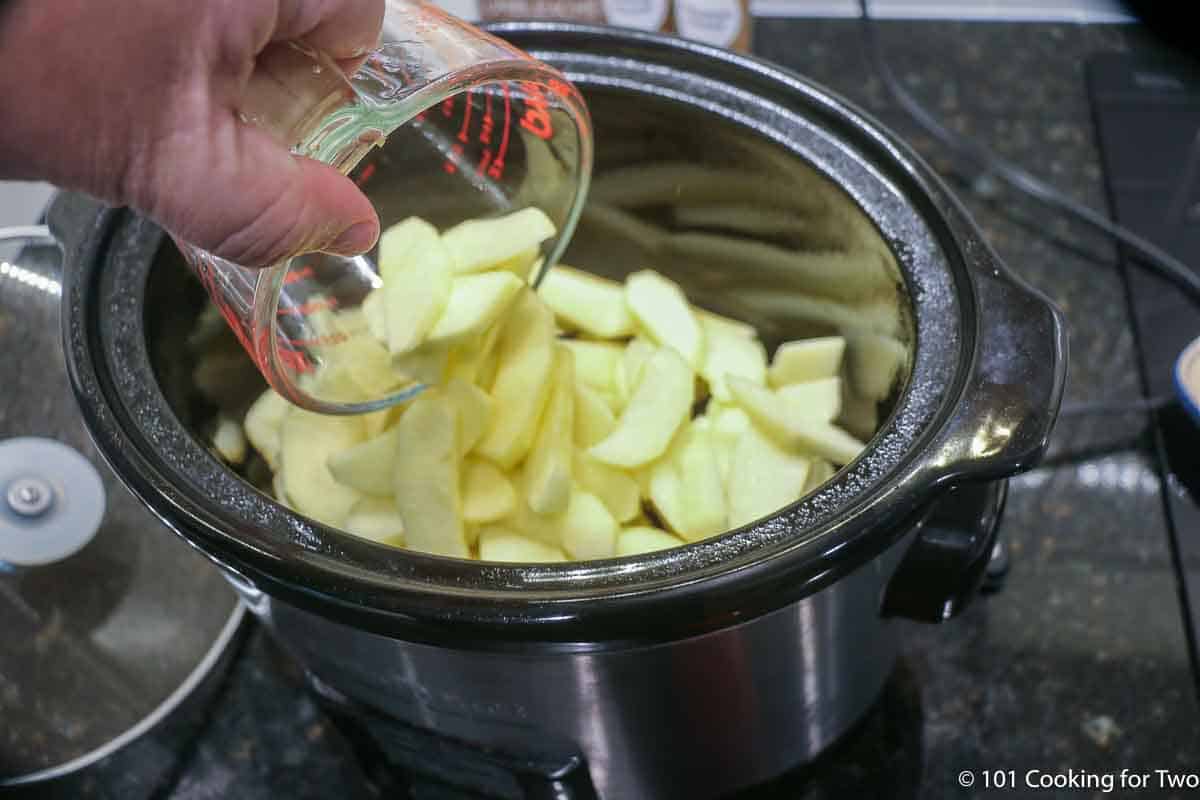 pouring apple slices into a crock pot.