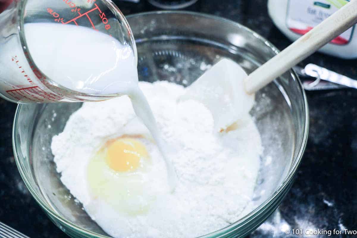 Pouring milk into bowl with flour and egg.