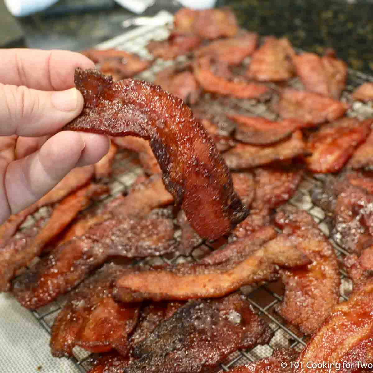 candied bacon being held above the tray.