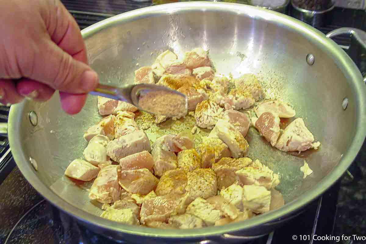 adding spices to cooking chicken.