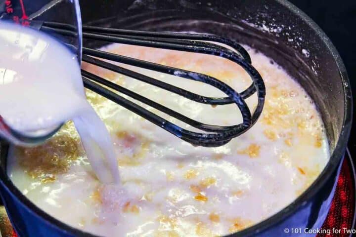 pouring milk into roux to make cheesy sauce.