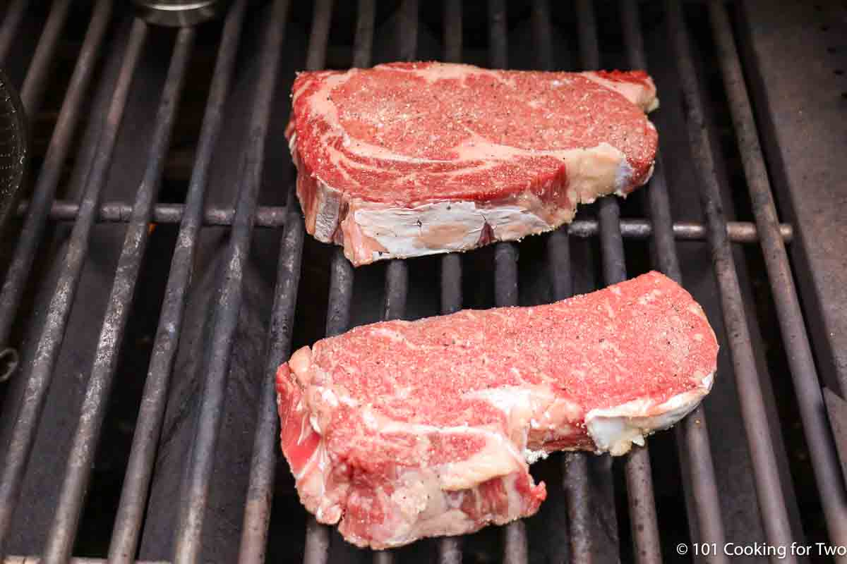 seasoned ribeye steaks on grill grates