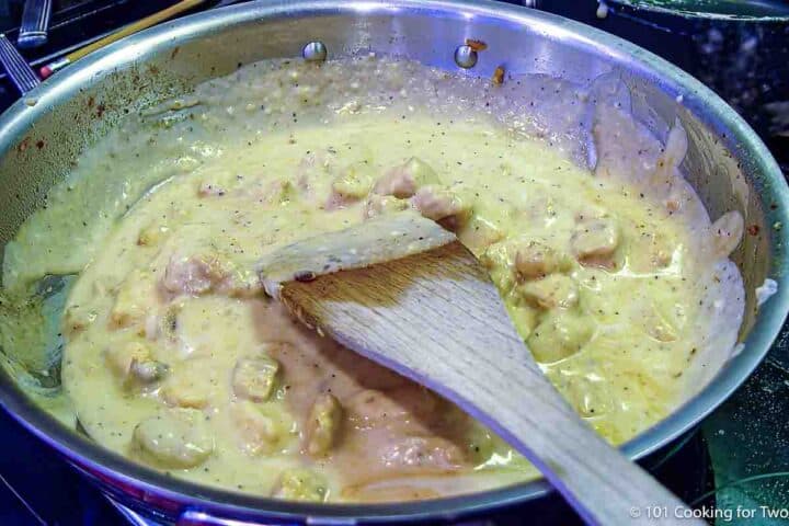 stirring chcken with alfrado sauce in pan.